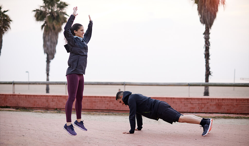 A woman and man doing bodyweight exercises outside.