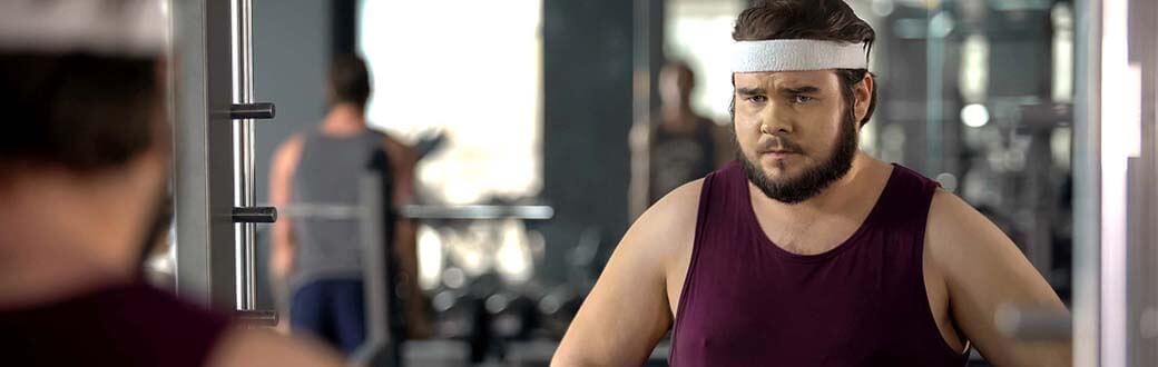 A man looking at himself in a mirror at a gym.