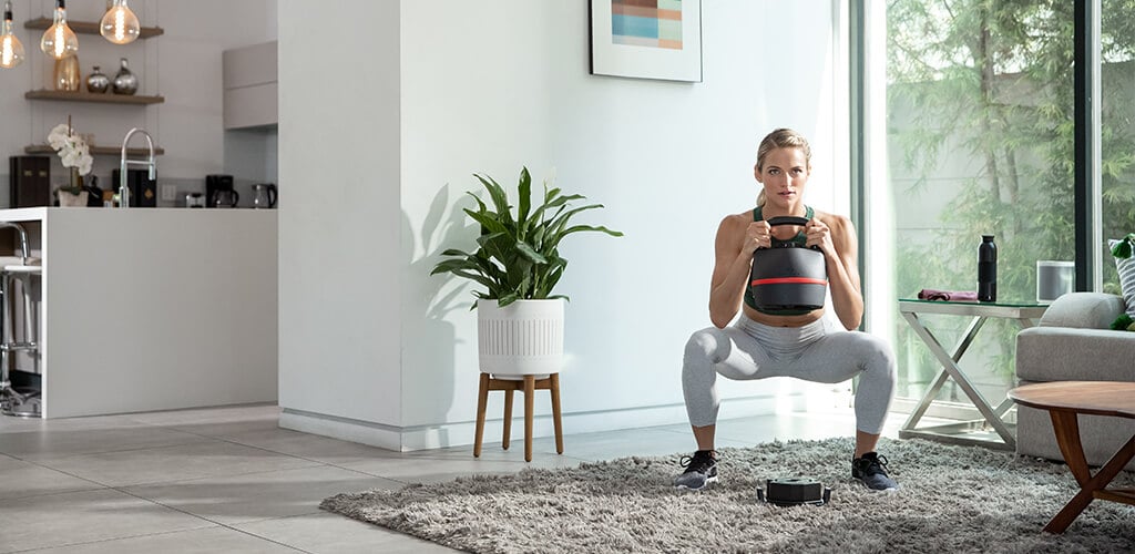 A woman performing a squat with an 840 adjustable kettlebell.