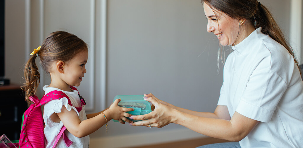 A mom handing lunch to her daughter.