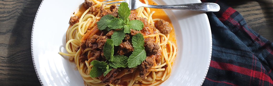 Plate of lamb Bolognese served on bucatini pasta.