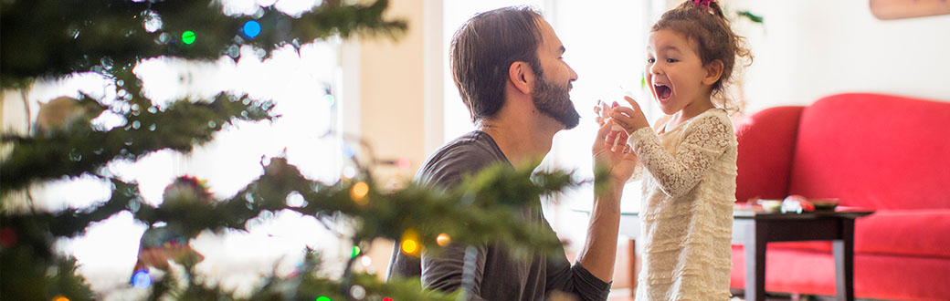 A father and daughter next to a Christmas tree.