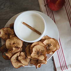 Baked apple slices on a plate surrounding a bowl of yogurt dip.