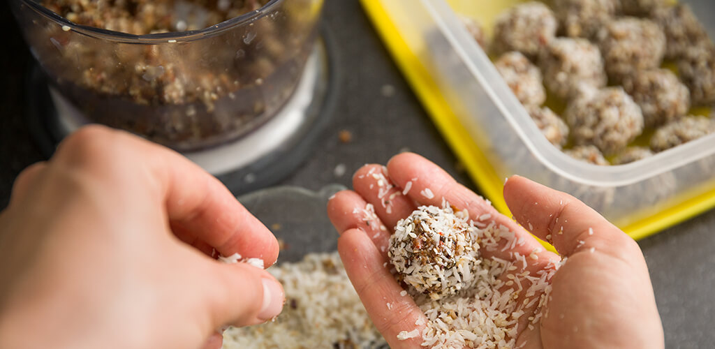 A person rolling an energy bite in shaved coconut.