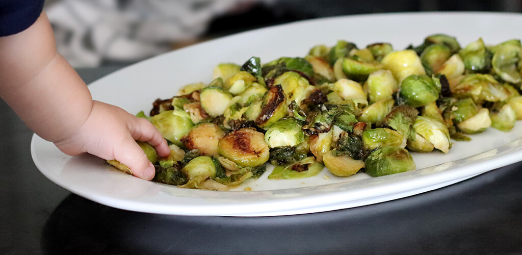 Child's hand picking up a Brussle sprout from a plate