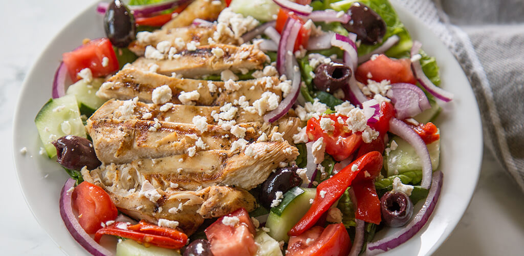 Greek marinated chicken over a greek salad on a table.