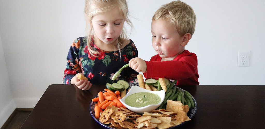 Two kids eating veggies and greek dip