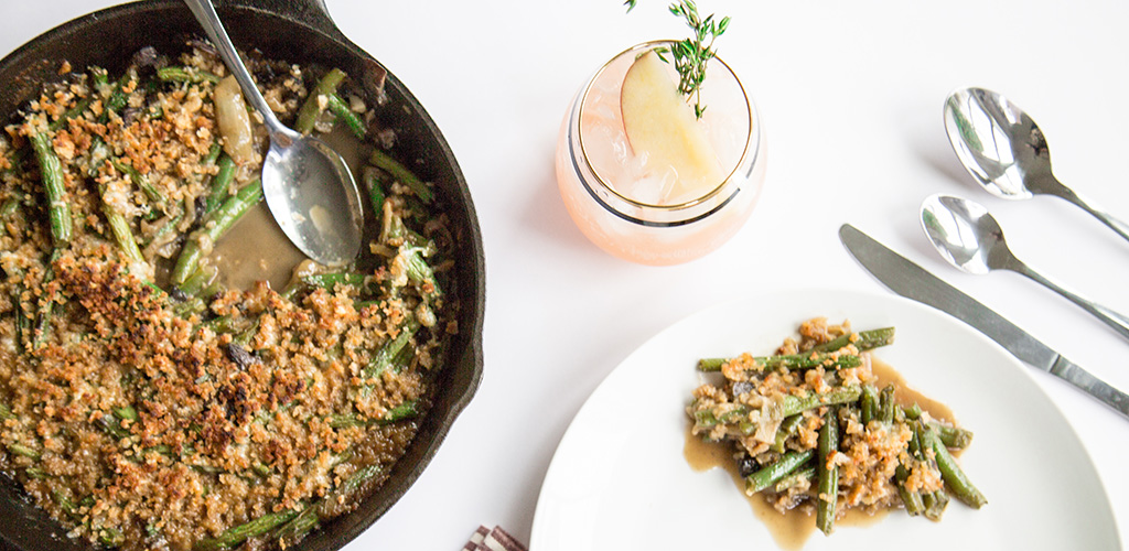 Green beans and caramelized onions in a skillet and on a plate next to a tasty looking drink.