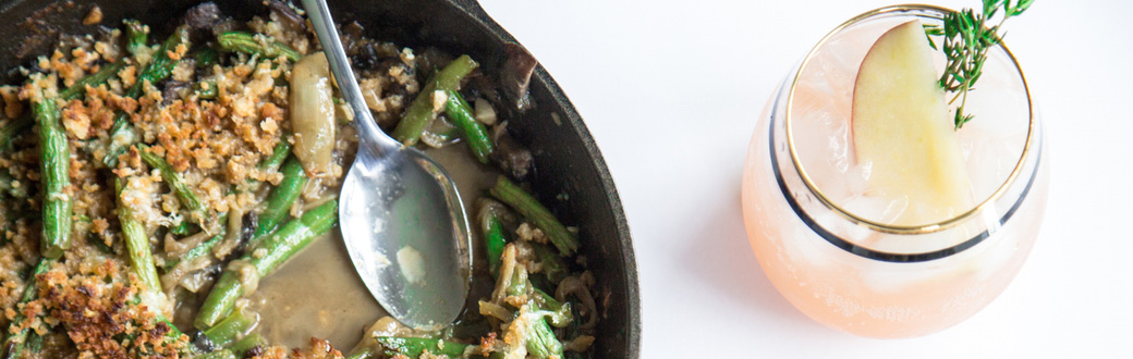 Green beans and caramelized onions in a skillet next to a cocktail.