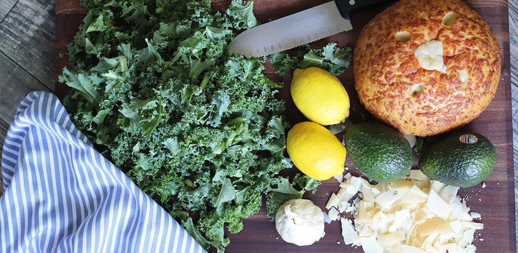 kale, lemon, avocado, garlic, grated cheese on a cutting board.