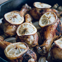 Roasted chicken legs topped with lemon slices in a cast iron skillet