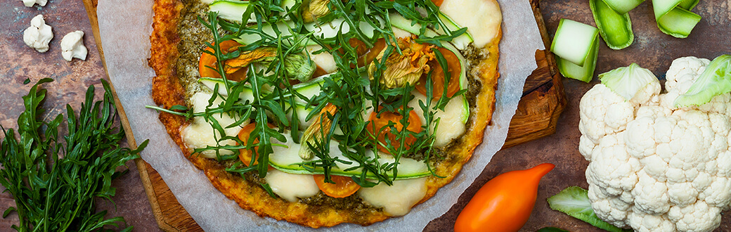 Pizza with cauliflower crust on a table with a head of cauliflower.