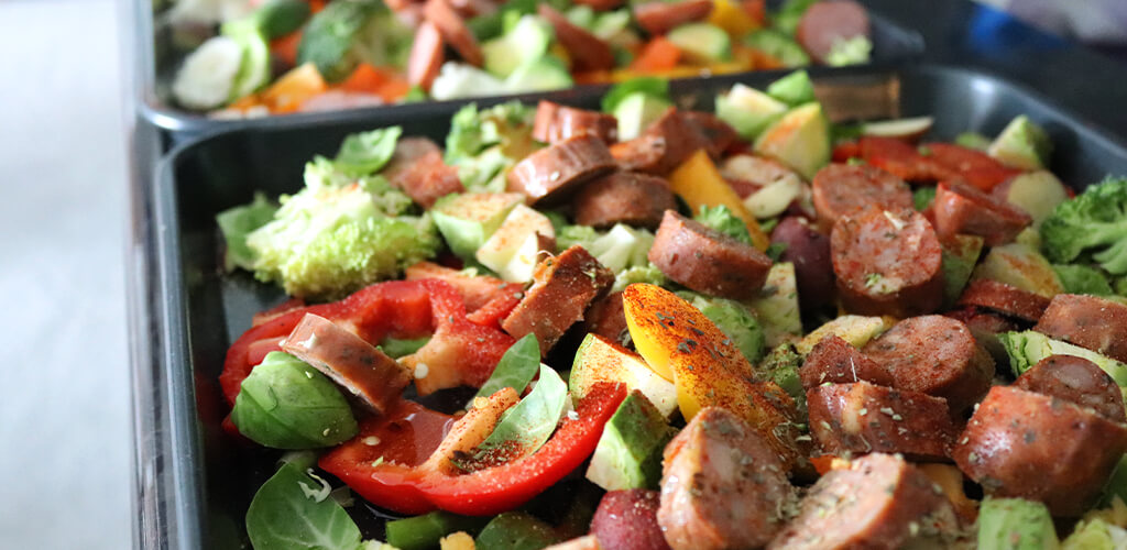 Assorted vegetables and sausage on a roasting pan.