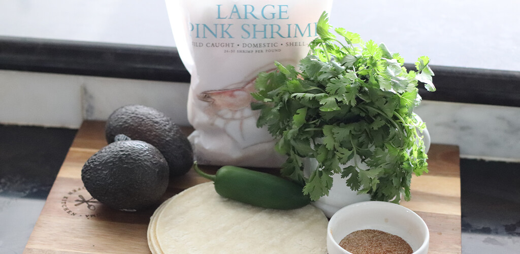 fresh cilantro, avocado, frozen shrimp, and spices on a cutting board.