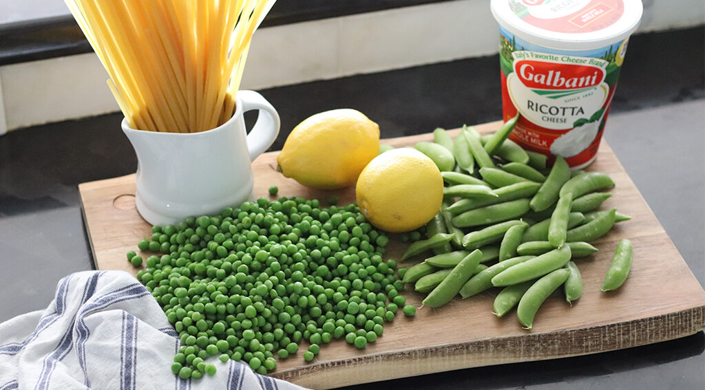 uncooked fettuccine, lemons, peas, snap peas, and ricotta on a cutting board.